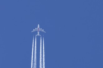 Airbus A380 jet passenger aircraft of Emirates airlines flying in a blue sky with contrails or