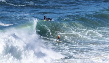 Surfers with their jet ski pilots in the Atlantic waves below Farol de Nazaré, Forte São Miguel,