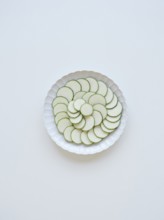 Thinly sliced zucchini arranged on a white plate, forming a visually appealing pattern of