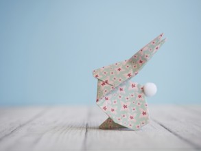 Floral origami easter bunny standing on a wooden table against a blue background