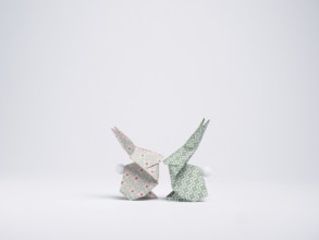 Two origami bunnies made with patterned paper are facing each other on a white background