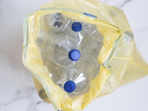 Plastic bottles with blue caps collected in yellow trash bag ready for recycling