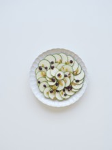 Thinly sliced zucchini arranged on a white plate, garnished with raisins and cranberries, creating