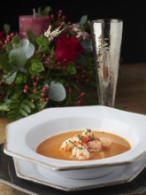 Shrimp bisque serving with prawns, chives, and foam, featuring a festive table setting