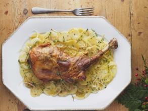 Whole roast leg of lamb with thinly sliced potatoes, onions, and fresh thyme sprigs