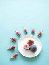 Figs, whole and sliced, arranged on a plate and around on a light blue background