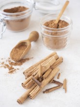Cinnamon sticks and ground powder in jars with a scoop on a white background