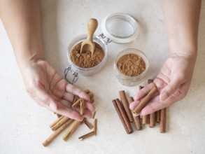 Hands holding two types of cinnamon sticks with ground spices in jars