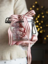 Woman holding a glass jar of red velvet cookies with a festive ribbon