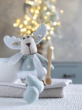 Fabric reindeer toy sitting with a wooden spoon and cozy christmas lights
