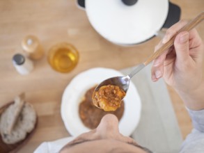 Woman holding a spoonful of lentil stew at lunch, top view of the table