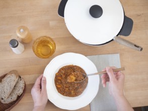 Woman eating a hearty lentil stew, served with whole wheat bread and a refreshing drink, creating a