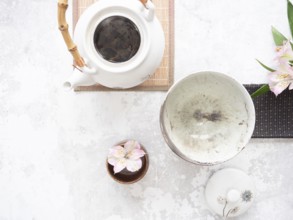 White teapot with bamboo handle, empty bowl, lid and pink flowers on light textured background are