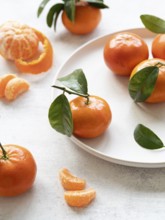 Vibrant tangerines with green leaves, showcasing freshness and citrusy appeal on a white plate and
