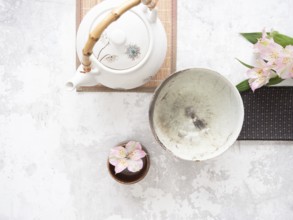 Asian tea ceremony arrangement with white teapot, empty bowl, pink flowers and bamboo placemat on