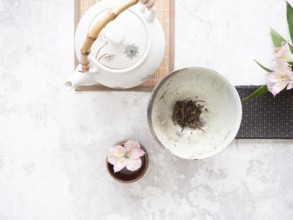 Traditional tea set with teapot, teacup, dried tea leaves, and pink alstroemeria flowers creates a