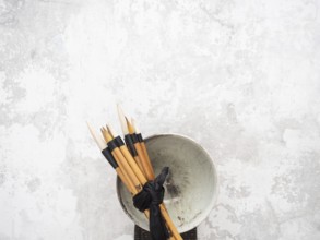 Multiple calligraphy brushes tied together with a black ribbon are resting on a ceramic bowl,