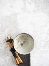 Calligraphy brushes tied with black ribbon and ceramic bowl resting on textured surface, creating