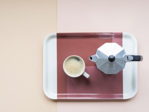 Coffee cup and moka pot sitting on a serving tray, minimalist flat lay on a pastel pink and beige