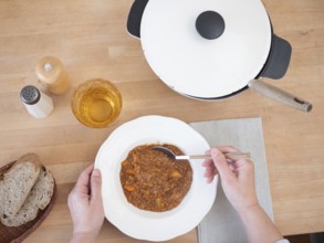 Woman enjoying a healthy and hearty lentil stew, accompanied by bread and a refreshing drink,