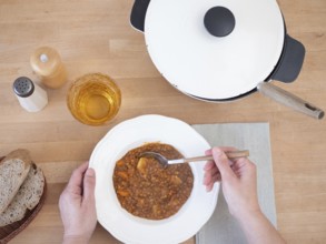 Woman eating a hearty lentil soup with whole grain bread and a glass of beverage, viewed from above