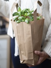 Woman holding a brown paper bag with fresh basil leaves, promoting sustainability and healthy