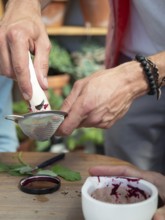 Hands filtering beetroot juice through a sieve, creating natural ink or pigment in a workshop