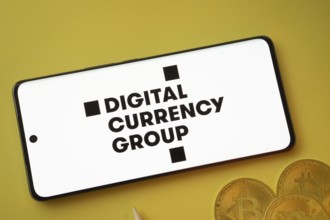 Dhaka, Bangladesh- 03 Oct 2025: Digital currency group logo on smartphone screen near Bitcoin coin