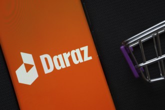 Dhaka, Bangladesh- 03 Oct 2025: A smartphone displaying the Daraz logo next to a miniature shopping