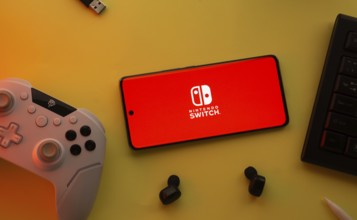 Dhaka, Bangladesh- 15 July 2025: Smartphone with nintendo switch logo, game controller, and earbuds