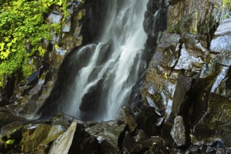 Vaucoux waterfall cascades gracefully over dark rocks, surrounded by lush greenery, Auvergne