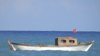 A small boat with a Turkish flag rocks calmly on the sea under a clear blue sky, Turkish Aegean