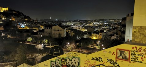 Nighttime city scene with glowing lights and graffiti along a wall, view of the city, Lisbon,
