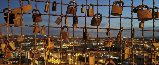 Metal grid full of love locks against an illuminated city backdrop in the evening, view of Lisbon