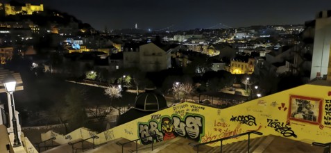 Night view of a long staircase, looking over Lisbon, with illuminated buildings and graffiti on a