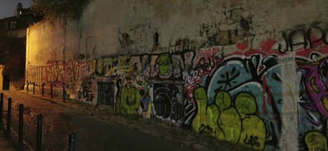 Graffiti-covered wall in a nighttime street scene with atmospheric street light, Lisbon, Portugal