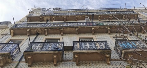 Old building with decorated balconies from which laundry hangs and tile façade under a blue sky,