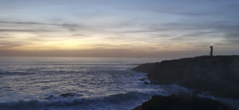 A lighthouse on the edge of the coast at sunset with waves in the sea, sunset over a peaceful ocean