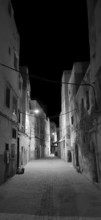 Black and white shot of a dark alley in Essaouira with sparse lighting and historic buildings,