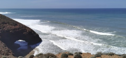 A picturesque coastline with a natural rock arch and strong waves in the blue ocean near Sidi Ifni,