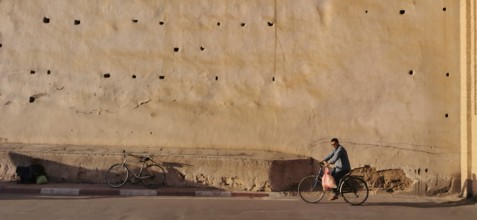 An old city wall with a cyclist riding along in the shade, Taroudannt, Morocco
