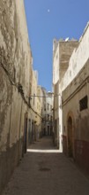 A narrow street lined with old buildings in Essaouira under a deep blue sky in an urban setting,