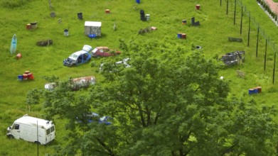 Green field with scattered car wrecks and barrels surrounded by trees, Poland