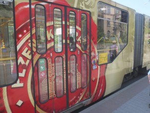 A tram with Pilsner Urquell painting stops at a sunny city stop, Pilsen, Czech Republic