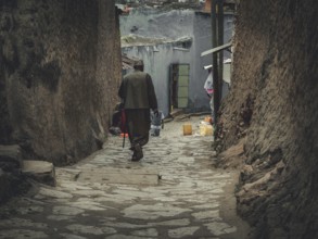 Man in a long coat walks through a narrow, stone-paved alley in Harar, Ethiopia