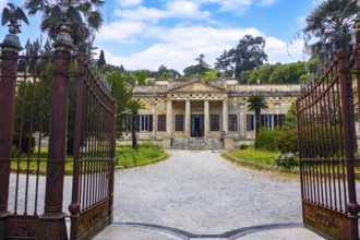 View through open old wrought-iron gate to main entrance with staircase and columned portal of