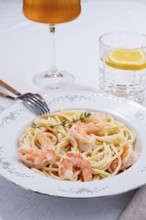 Pasta with shrimp and thyme, served on a white plate, with a glass of white wine, the table is set,