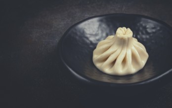 One khinkali, on a black plate, top view, cooking concept, Georgian cuisine