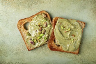 Two slices of toasted bread, topped with pistachio paste and sprinkled with pistachios, spread on a