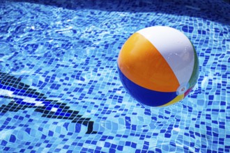 Colorful beach ball floats on the surface of a pool reflecting sunlight on a summer day